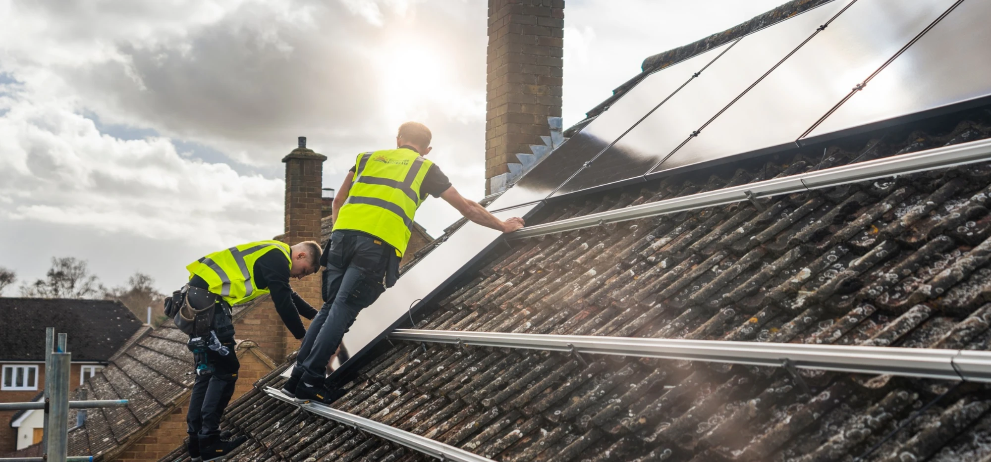 Two Greenscape installers fitting solar panels on a tiled roof