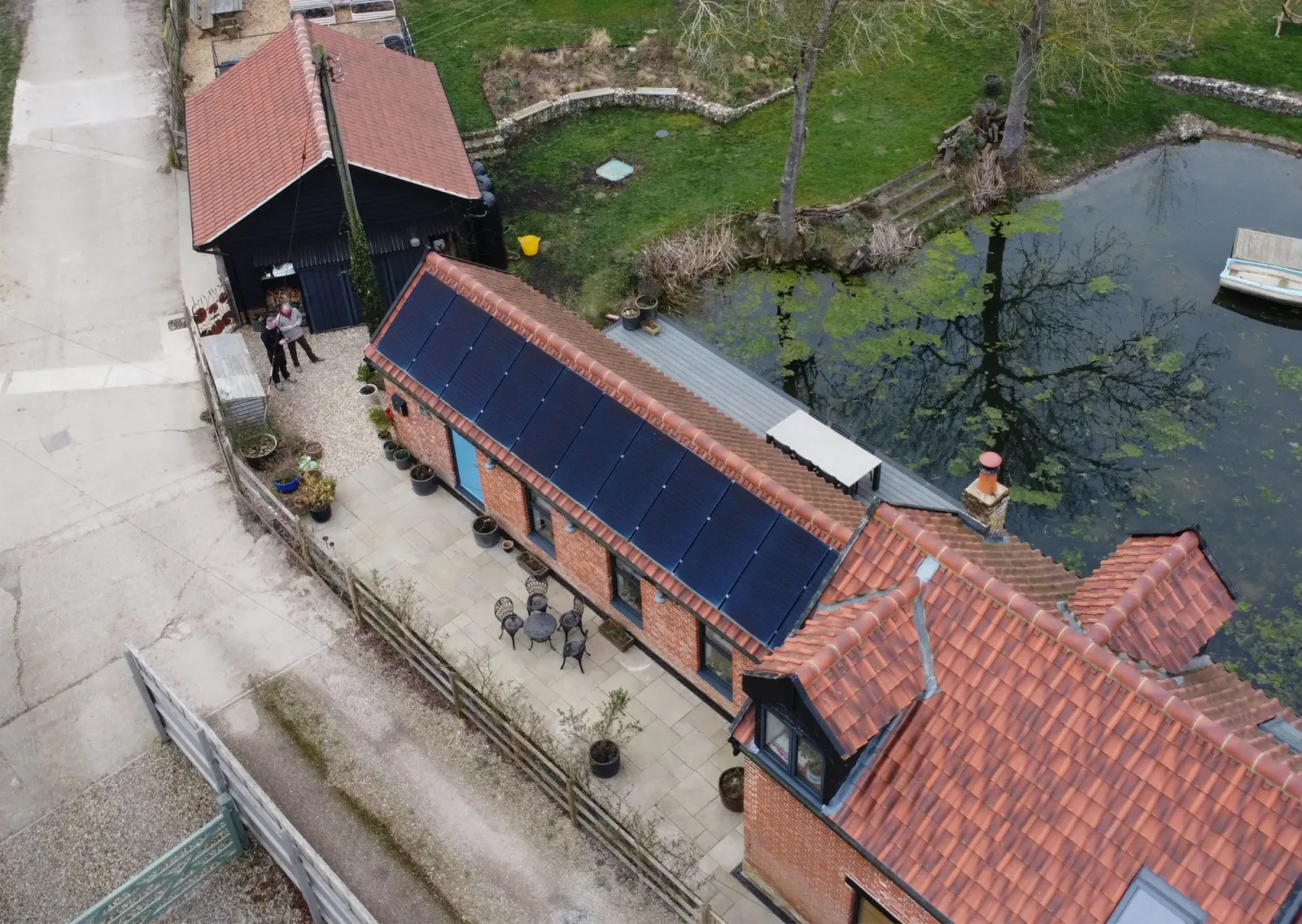 Aerial view of Nick's barn conversion beside the pond, with black solar panels on its tiled roof