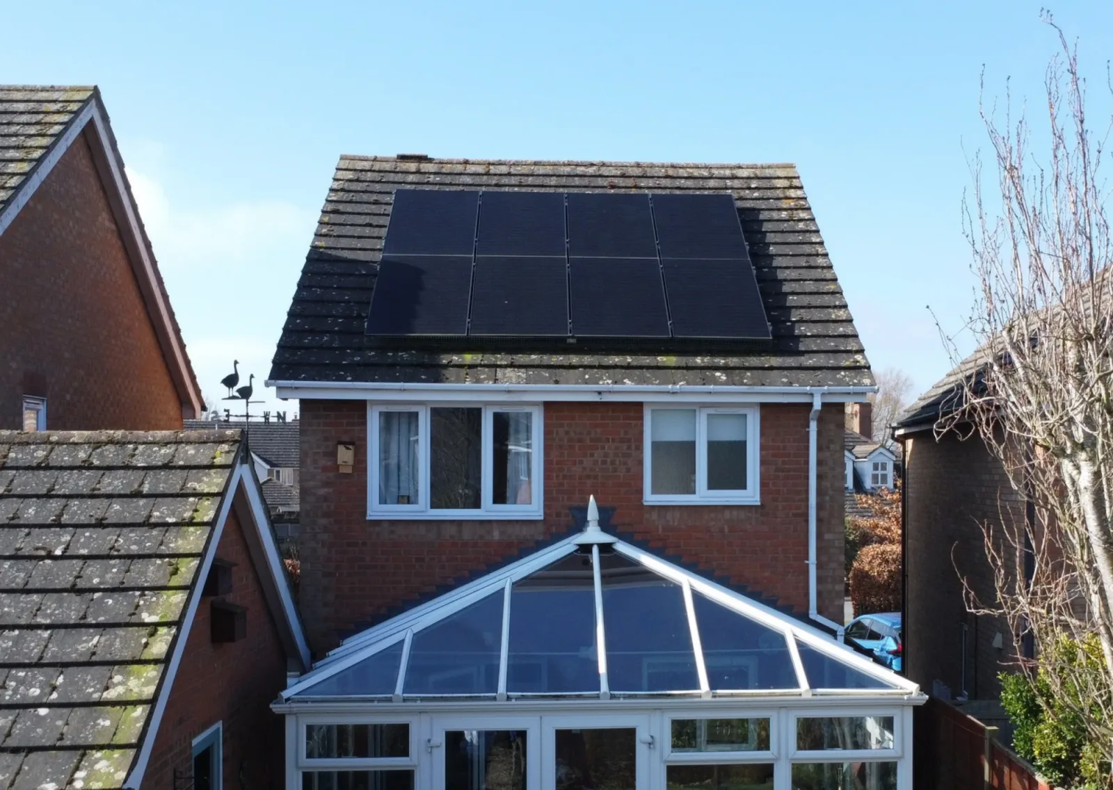 A detached brick house with black solar panels on its tiled roof and a conservatory