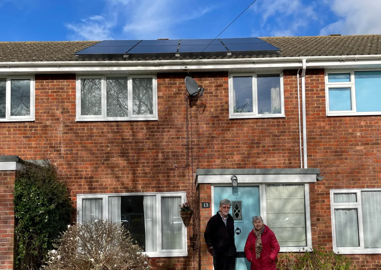 Jonathan and Jane outside their brick home with eight black solar panels on the roof