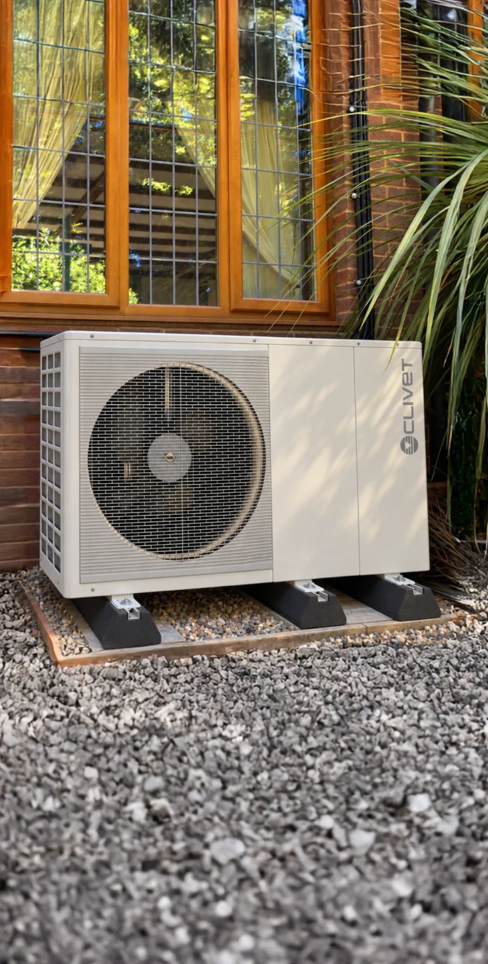A Clivet heat pump beneath a leaded window, with a palm plant beside it