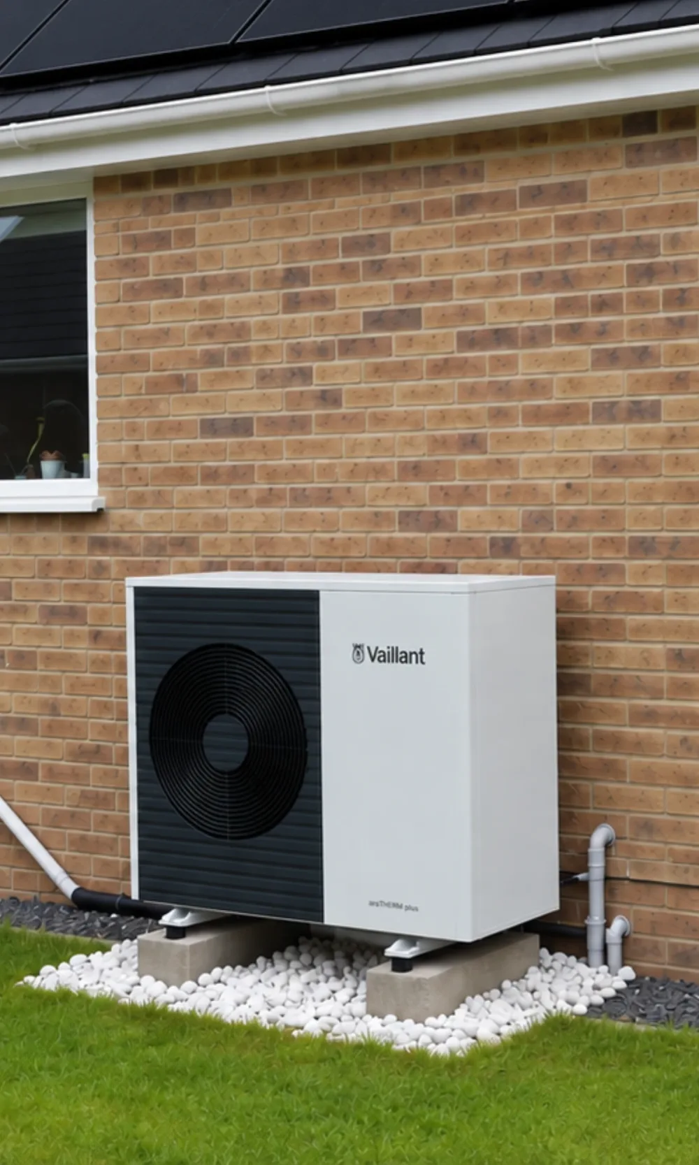 A Vaillant aroTHERM Plus heat pump on a buff-brick wall with white pebbles around its base