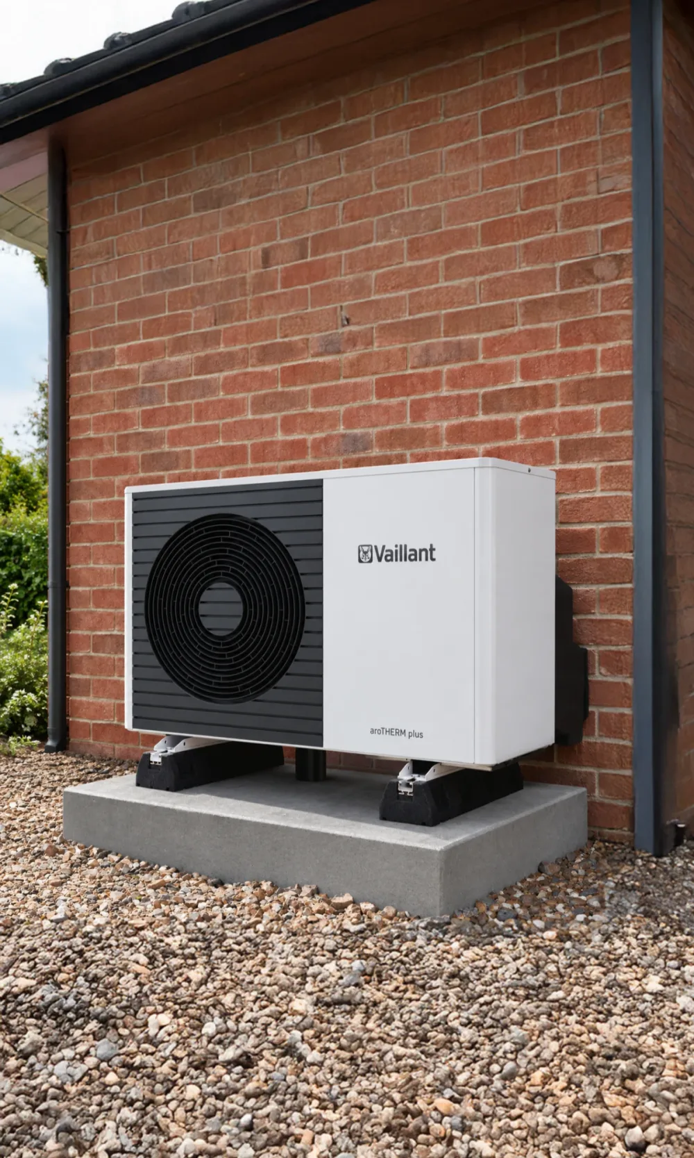 A Vaillant aroTHERM Plus heat pump on a concrete plinth against red brick, with gravel in front