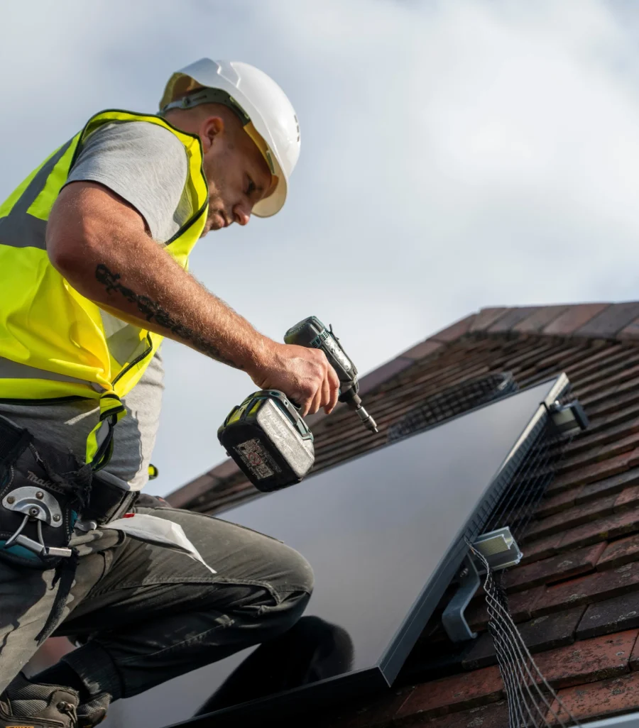 An installer in a hard hat fitting a solar panel with a cordless drill