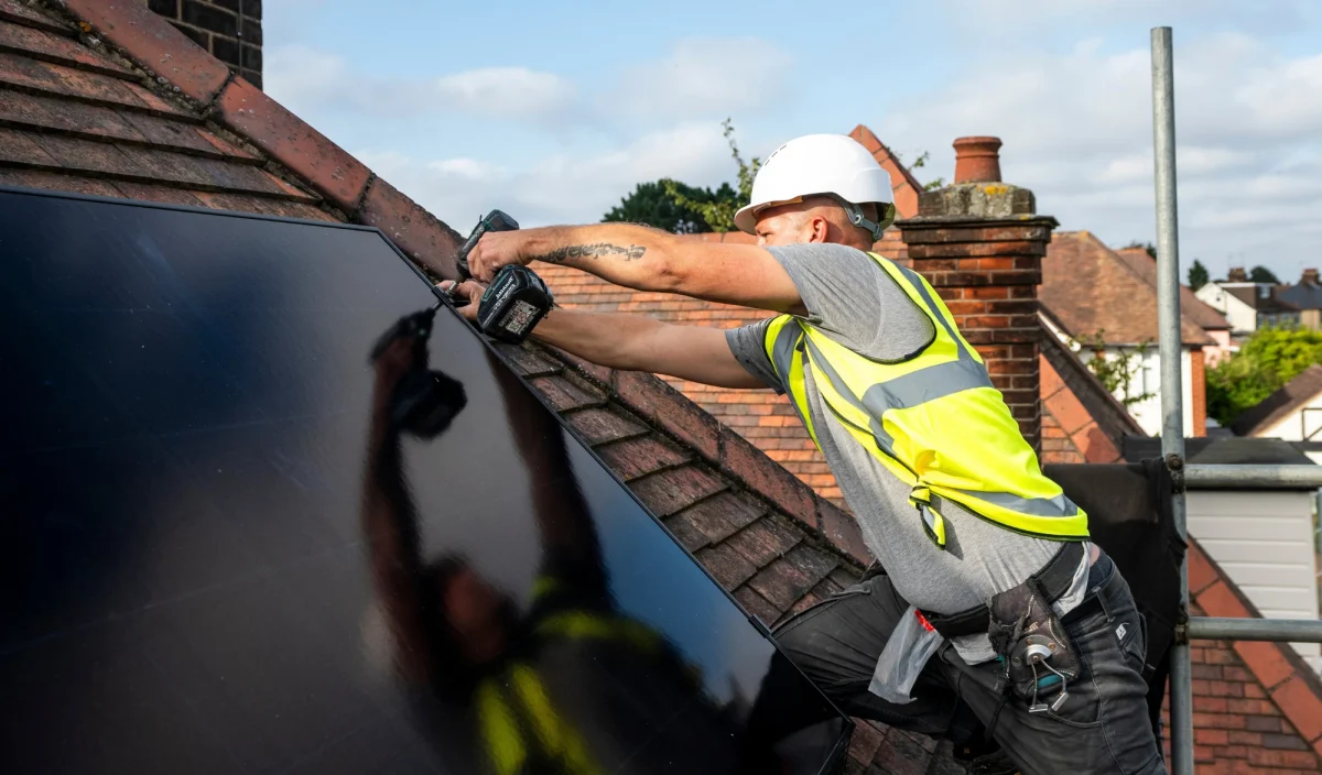 An installer fitting a solar panel to a roof with a cordless drill