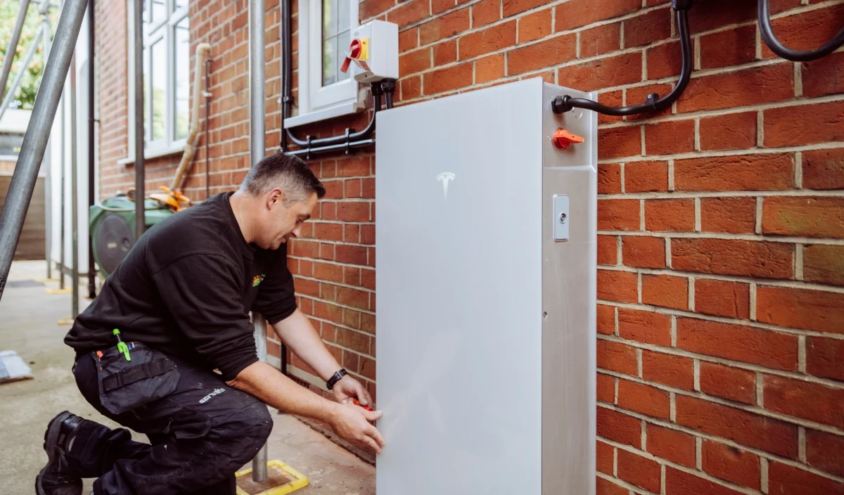 An engineer installing a Tesla Powerwall battery on a brick wall