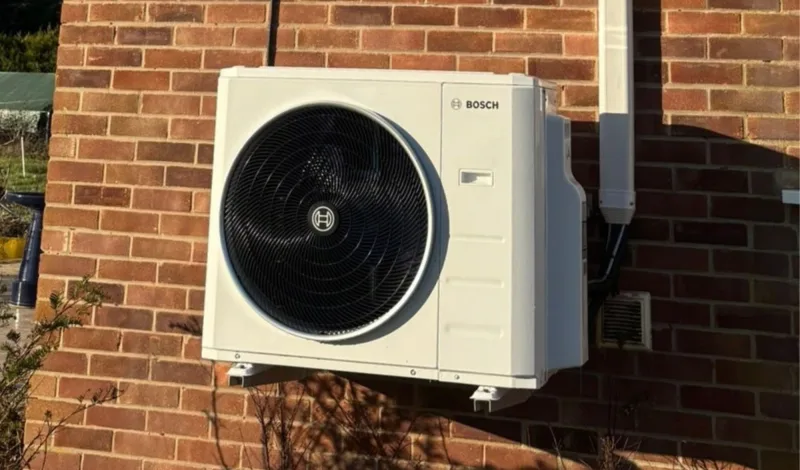 A Bosch outdoor unit on a red-brick wall beside a white downpipe