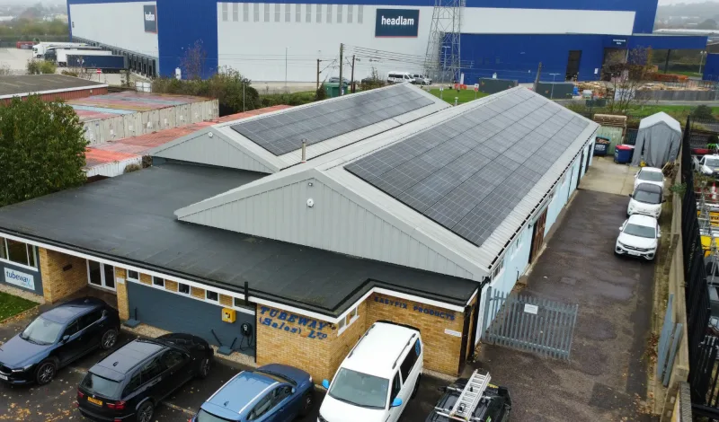 An aerial view of a small business unit with two roofs of solar panels, with a large distribution warehouse behind