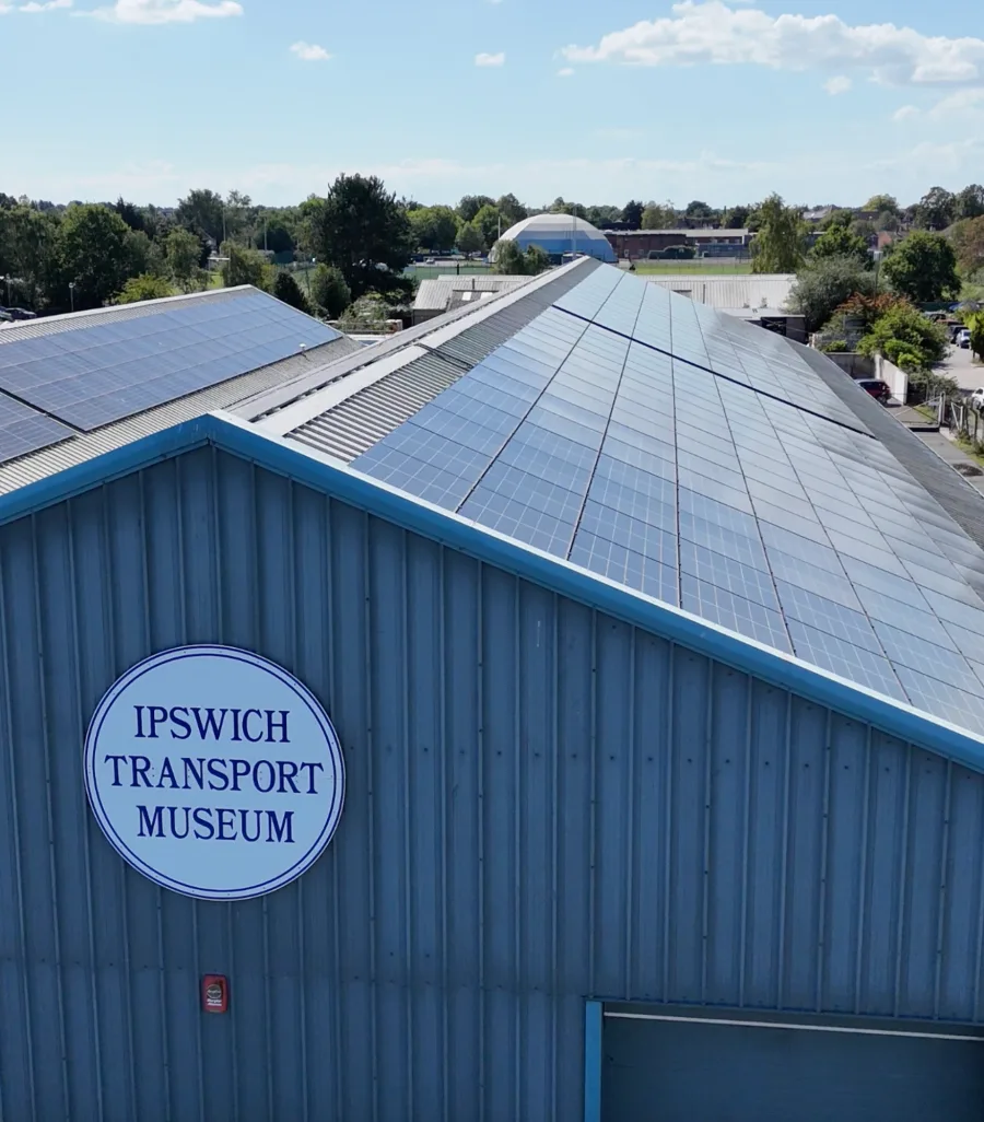 Rows of solar panels on the roof of the Ipswich Transport Museum, seen over its blue-trimmed gable with the museum's round sign