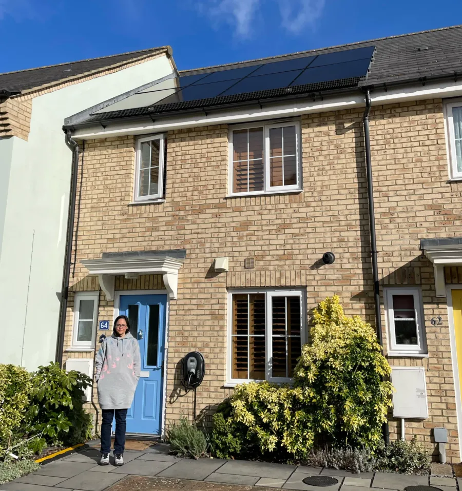 A homeowner standing outside her buff-brick terrace with a solar roof, a blue front door and an EV charger