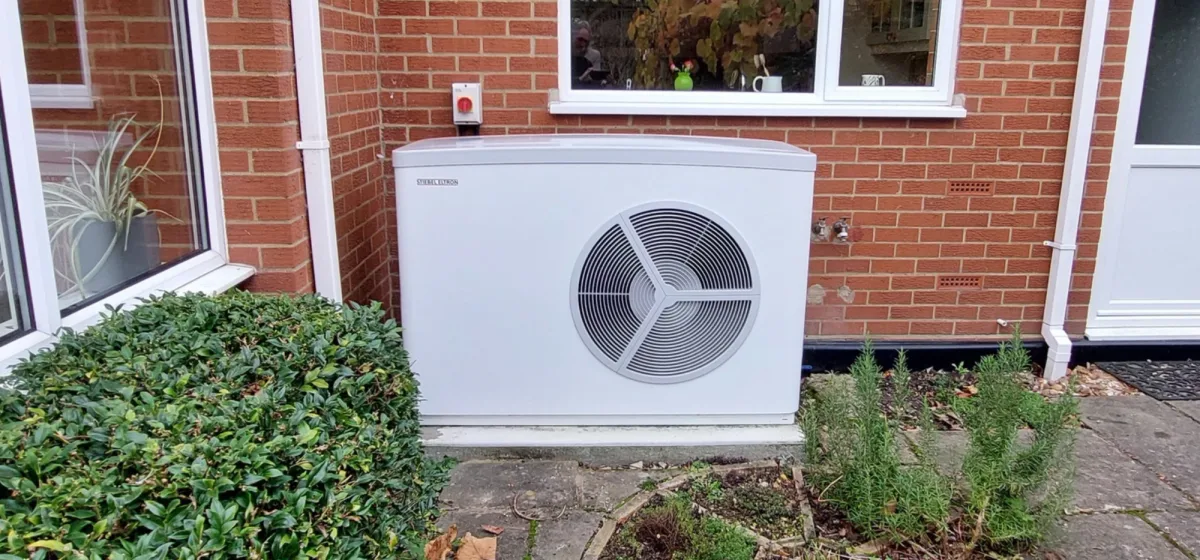 A Stiebel Eltron heat pump against a red-brick wall beside a hedge