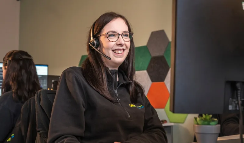 A smiling Greenscape team member in a headset at her desk in the office