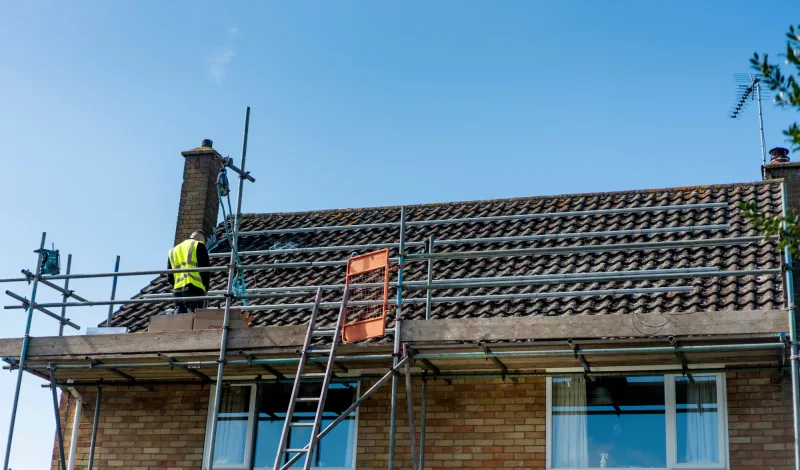 A Greenscape installer on scaffolding beside a roof with mounting rails fitted