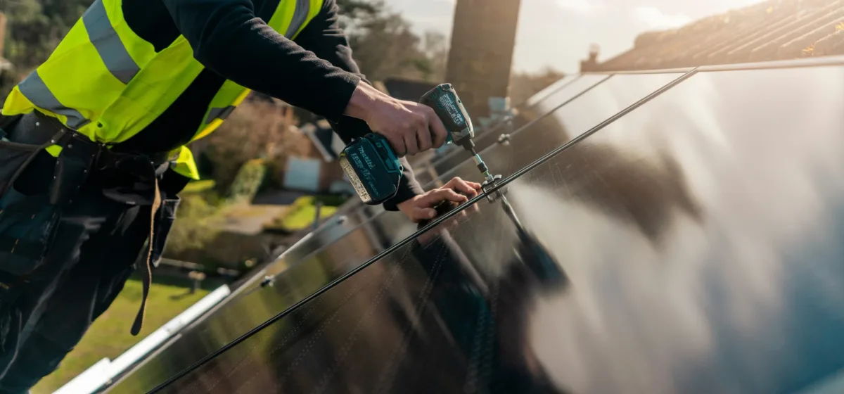 A Greenscape installer in hi-vis fixing a solar panel to a roof with an impact driver