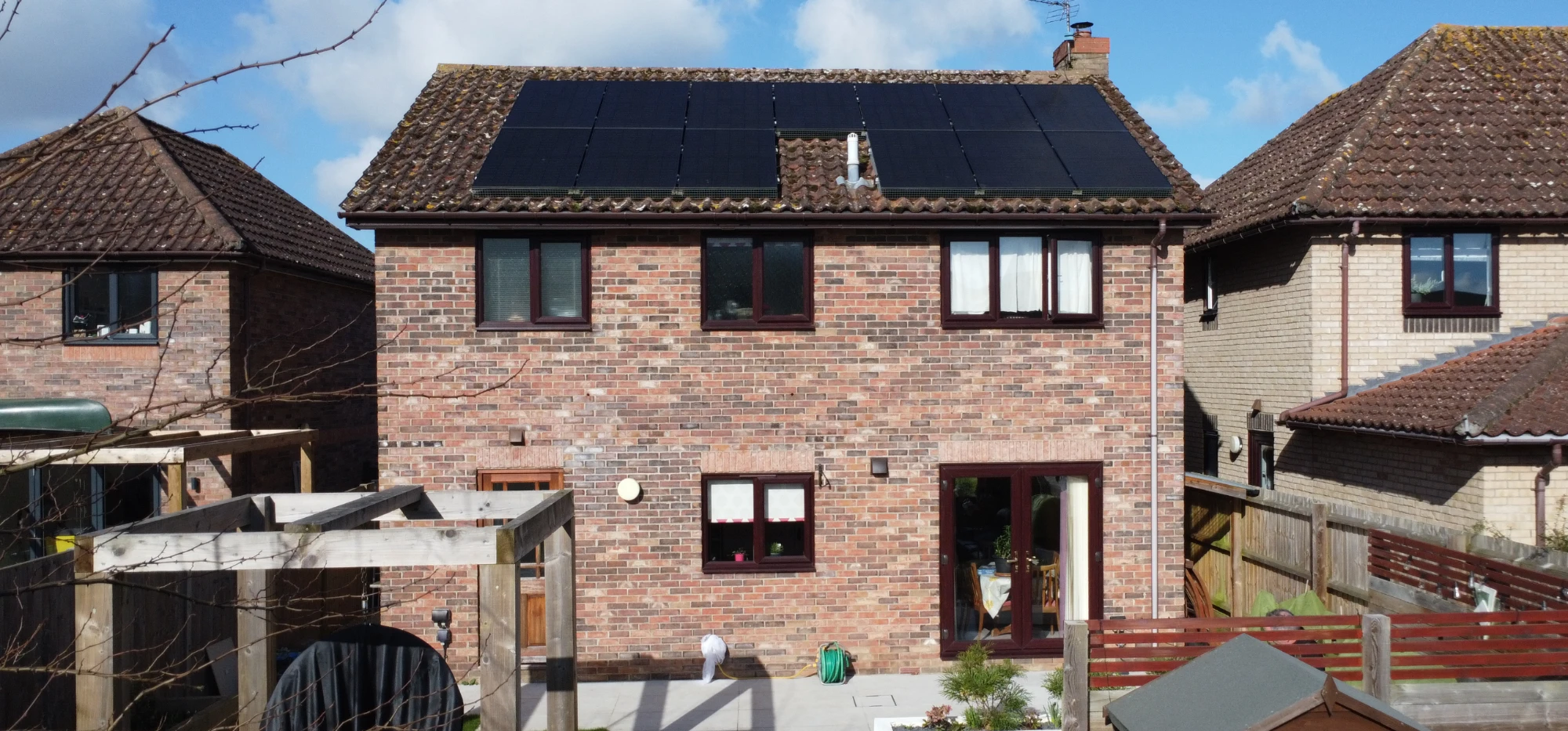 A brick house with a full roof of solar panels, seen from the garden