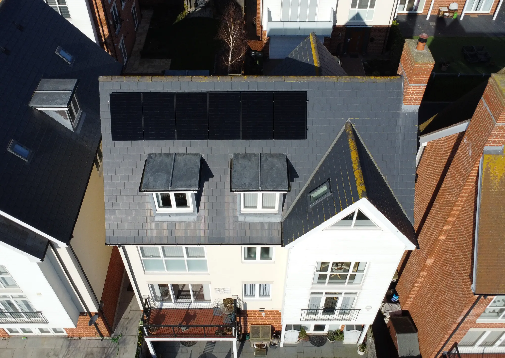 Greenscape installers fitting solar panels to a tiled roof in bright sunshine