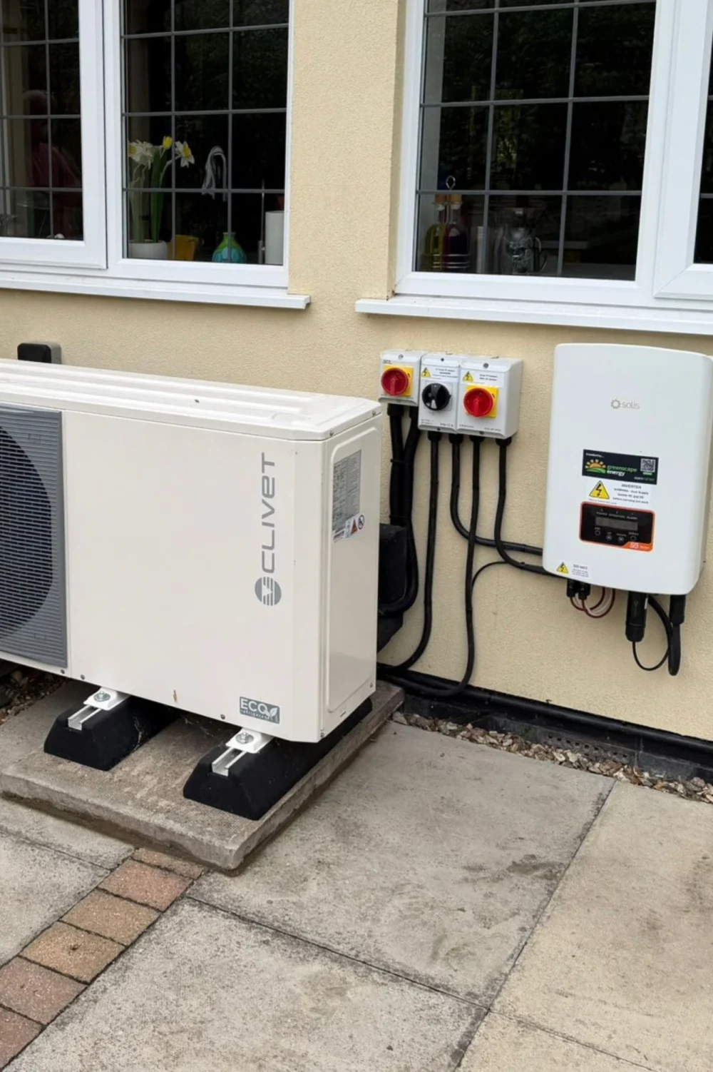 A Clivet heat pump beside three isolators and a Solis inverter on a cream rendered wall