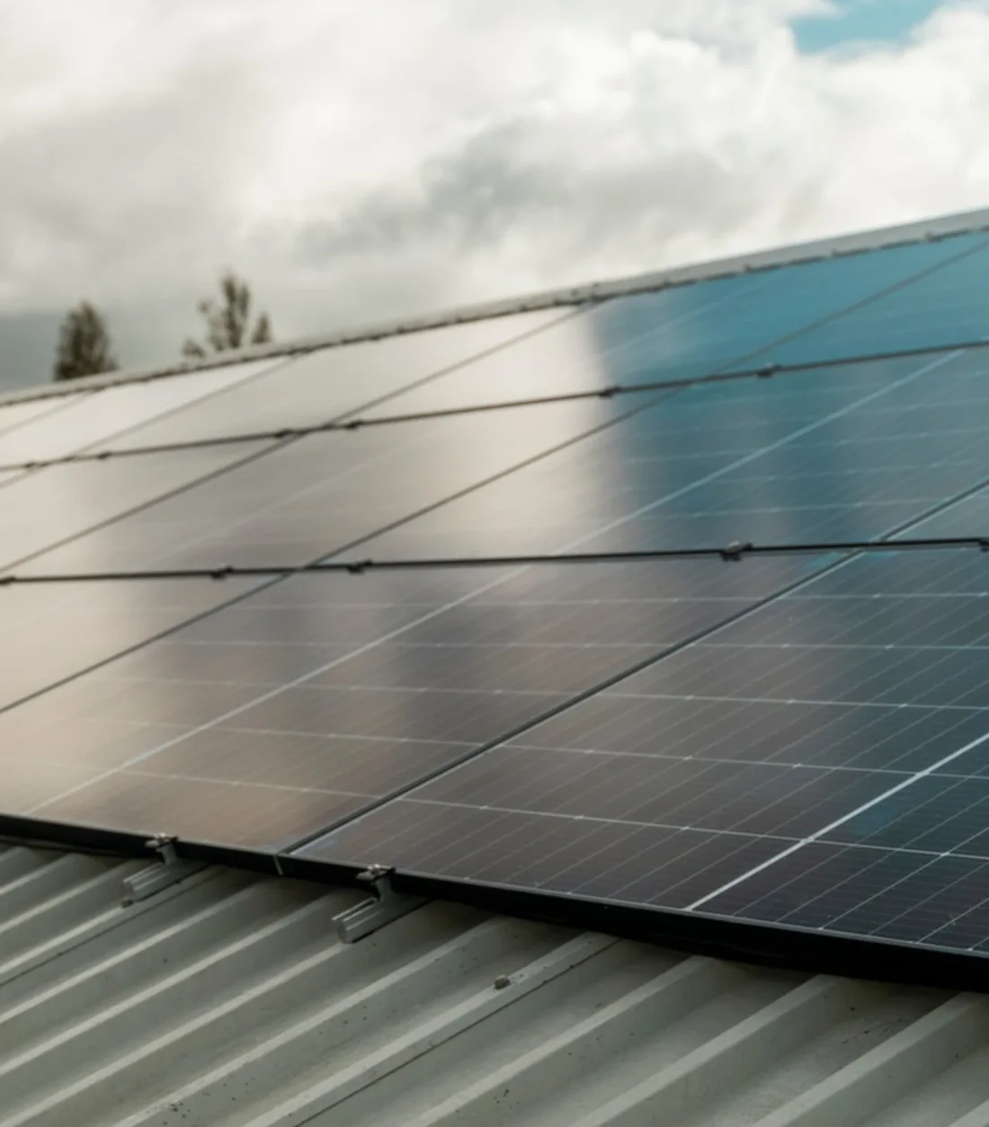 Black solar panels on a corrugated metal roof under a cloudy sky